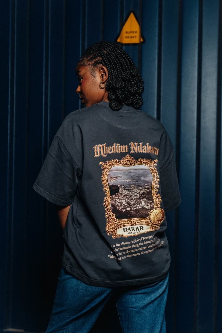 Dos d’un t-shirt Mbedüm Ndakaru imprimé Dakar, devant un conteneur bleu
